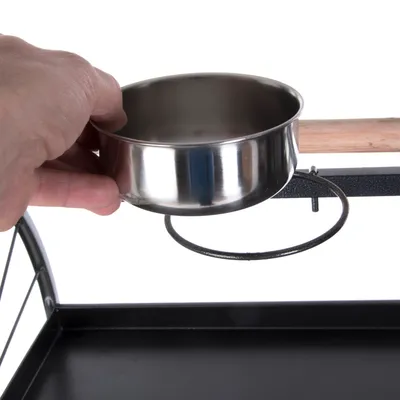 Ruka umisťuje nerezovou misku do kovového držáku na dřevěném stojanu. Produkt představuje krmící příslušenství pro domácí mazlíčky.