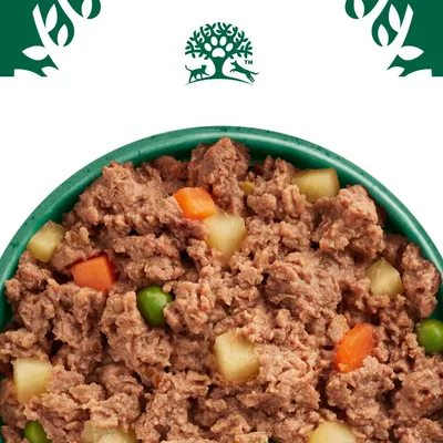 Close-up of wet food with meat pieces, carrots, peas and potatoes in a green bowl. Logo with tree and animals visible at the top.