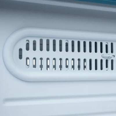 Detailní záběr na bílou ventilační mřížku s horizontálními štěrbinami, vhodnou pro ventilační systémy v přepravkách pro zvířata.