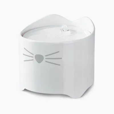 Fontaine à eau blanche en céramique, forme de tête de chat avec oreilles et motif museau et moustaches, jet d’eau visible au centre.