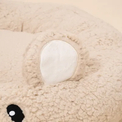 Nahaufnahme eines runden, beigen Kuschelbetts aus Plüsch mit aufgenähter Ohr- und Augenapplikation. Nahaufnahme eines runden, beigen Kuschelbetts aus Plüsch mit aufgenähter Ohr- und Augenapplikation.