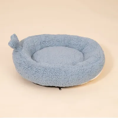 Rundes, hellblaues Kuschelbett mit weichem Plüschbezug und erhöhtem Rand, seitlich mit Stoffohr-Applikation.