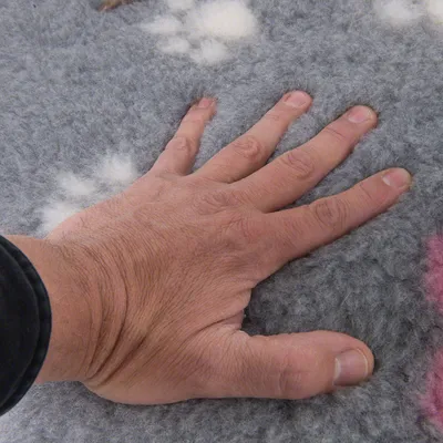 Hand drückt auf grauen, weichen Stoff mit weissen Pfotenmustern zur Demonstration der Materialbeschaffenheit.