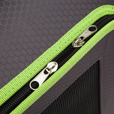 Dettaglio di una cerniera doppia in metallo con bordo verde su tessuto grigio a nido d'ape, parte di un trasportino o borsa per animali.