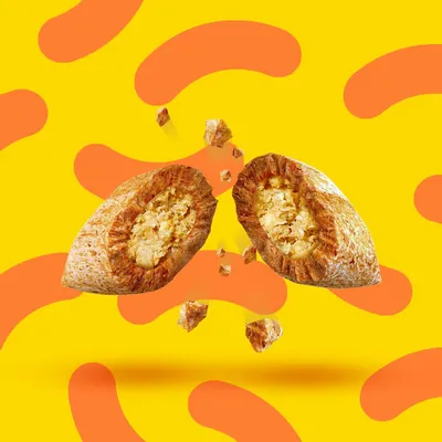 Croquette pour animal coupée en deux, montrant l’intérieur avec une garniture claire, morceaux visibles autour, fond jaune à motifs orange. Marque et texte non visibles.