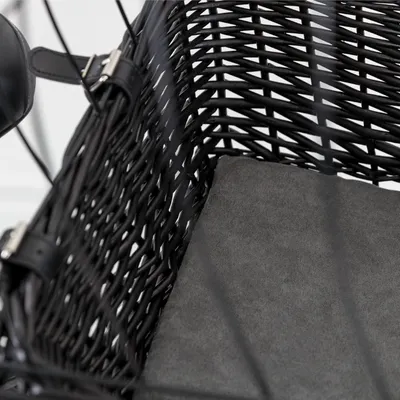 Panier en osier noir avec coussin gris, attaches en cuir noir et boucles métalliques visibles sur le côté.