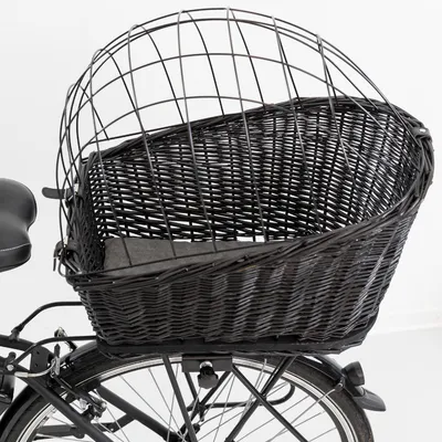Panier en osier noir avec grille métallique, fixé à l’arrière d’un vélo, coussin gris visible au fond du panier.