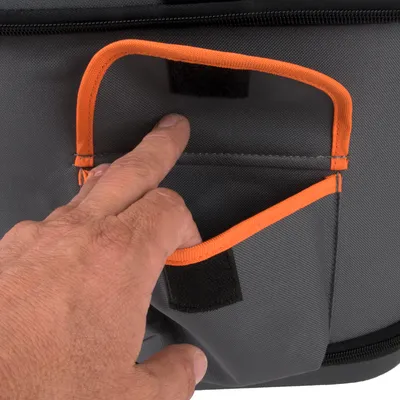 Main ouvrant une poche en tissu gris avec bordure orange et fermeture velcro noire sur un sac ou accessoire.