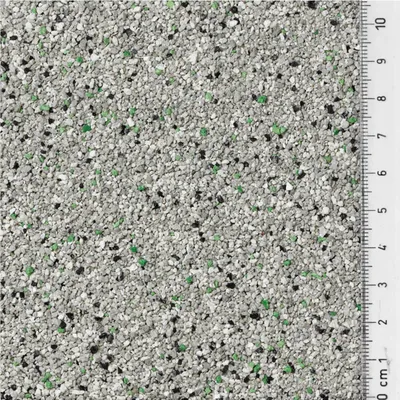 Nahaufnahme von grauem Katzenstreu mit grünen und schwarzen Partikeln, Maßstab in Zentimetern sichtbar von 0 bis 10 cm.
