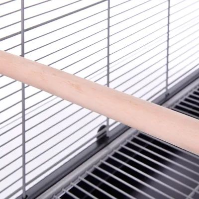 Barra de madera colocada en el interior de una jaula metálica para aves, con base y barrotes visibles.