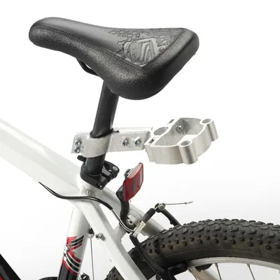 Soporte metálico montado bajo el sillín de una bicicleta blanca, fijado con tornillos. Se observa parte del cuadro, la rueda trasera y un reflector rojo.