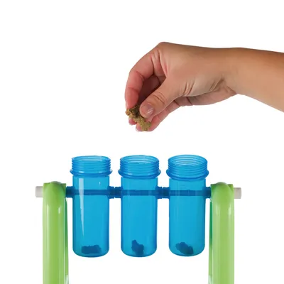 Hand plaatst hondensnoepjes in drie blauwe kunststof buisjes op een groen interactief voerspeelgoed.