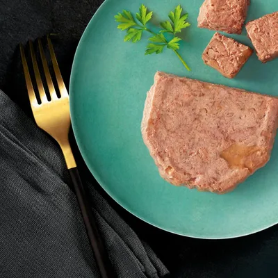 Portion of wet pet food served on a plate, with several small cubes and parsley garnish shown for texture and serving suggestion.