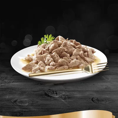 Piatto bianco con bocconcini di carne in salsa, decorato con foglia verde e posate dorate accanto. Nessun marchio o testo visibile.