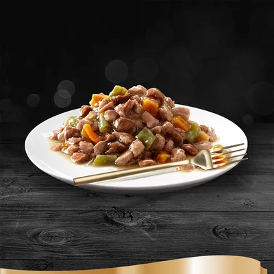 Piatto bianco con bocconcini di carne in salsa, visibili pezzi di verdure arancioni e verdi, forchetta dorata accanto. Nessun marchio o testo visibile.