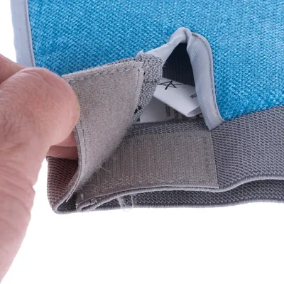 Nahaufnahme eines blauen und grauen Stoffprodukts mit Klettverschluss, geöffnet von einer Hand. Sichtbar sind Etiketten im Inneren.