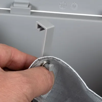 Hand bevestigt grijze kunststof haak aan metalen oogje van een zilverkleurige zak, detailopname van sluitmechanisme of ophangsysteem.