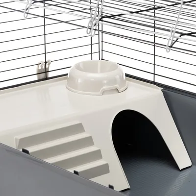 Kleintierkäfig mit Kunststoffplattform, integriertem Fressnapf, Treppe und Unterstand. Metallgitter mit Hakenverschluss sichtbar.