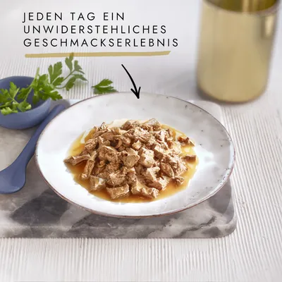 На изображении тарелка с сочными кусочками мяса в соусе, украшенная петрушкой и синим ложкой.