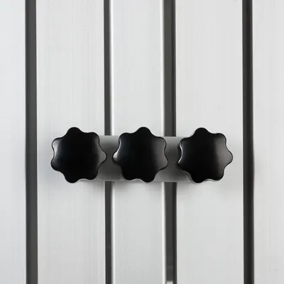 Dettaglio di tre manopole nere a forma di fiore su una barra in metallo argentato, montate su superficie verticale a doghe grigie.