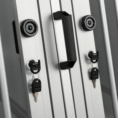 Dettaglio di struttura in metallo con maniglia nera centrale, due serrature con chiavi inserite e due manopole nere laterali. Materiale: metallo e plastica visibili.