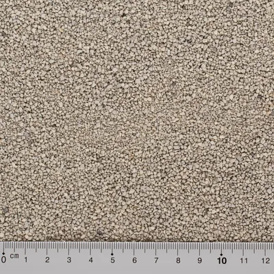 Nærbillede af lysegrå kattegrus med kornstørrelse vist ved lineal i centimeter fra 0 til 12 nederst i billedet.