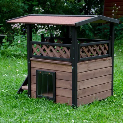 Drvena kućica za kućne ljubimce s krovom, prozorčićem od prozirne plastike i ogradom na gornjoj terasi. Kućica stoji na travi na otvorenom.