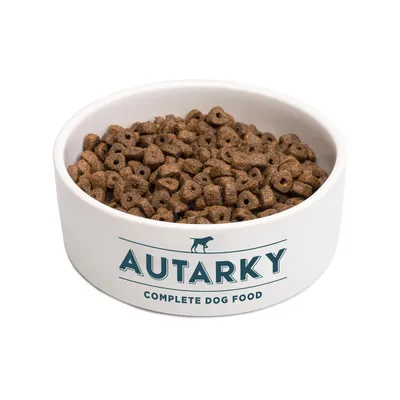 Bowl filled with brown dry food pieces, labelled 'Autarky Complete Dog Food' on the front of the bowl.