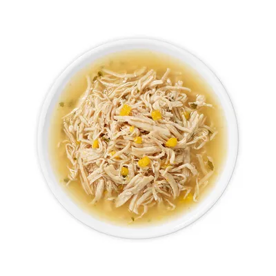 Close-up of shredded chicken with yellow vegetable cubes in broth, served in a white bowl.