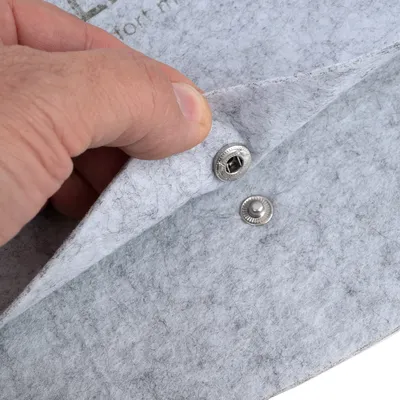 Detailaufnahme eines grauen Filzmaterials mit Druckknopfverschluss, gezeigt durch eine Hand, die den Stoff anhebt.