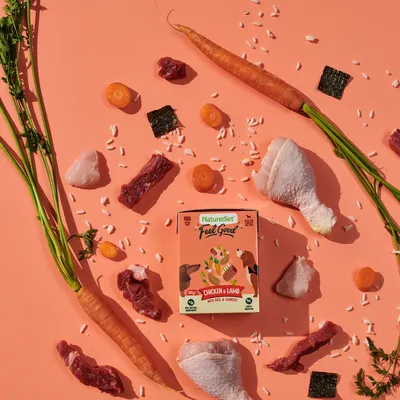 Product image showing Naturediet Feel Good Chicken & Lamb with rice and carrots, surrounded by raw chicken, lamb, carrot pieces, rice grains, and seaweed.