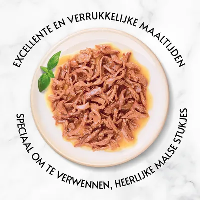 EXCELLENTE EN VERRUKKELIJKE MAALTIJDEN. SPECIAAL OM TE VERWENNEN, HEERLIJKE MALSE STUKJES staat rond een bord met natvoer in saus en een basilicumblaadje.