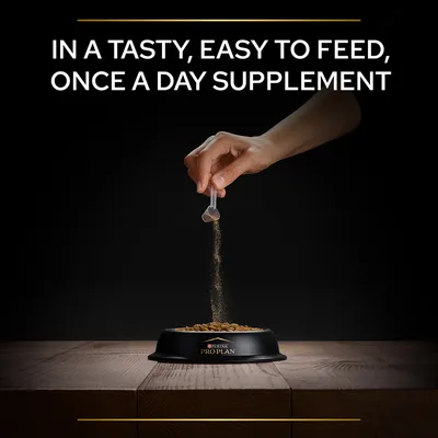 Hand sprinkling powder from scoop over kibble in a Purina Pro Plan bowl. Text: IN A TASTY, EASY TO FEED, ONCE A DAY SUPPLEMENT.