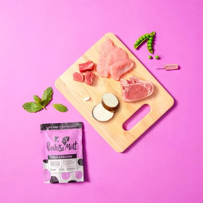 Image showing meat cuts, peas, sweet potato, mint leaves, a capsule and a sachet of Pooch & Mutt Calm & Relaxed food, highlighting visible ingredients in the product.