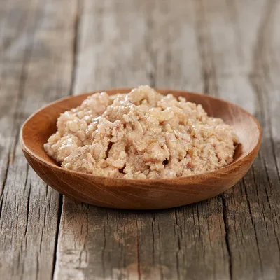 Pâtée pour animaux servie dans une assiette en bois, texture humide et morceaux visibles, sans marque ni texte apparent.