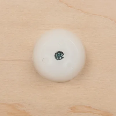 Kulatá bílá plastová krytka se středovým šroubem na dřevěném povrchu, vhodná pro montáž nábytku nebo příslušenství. Kulatá bílá plastová krytka se středovým šroubem na dřevěném povrchu, vhodná pro montáž nábytku nebo příslušenství.