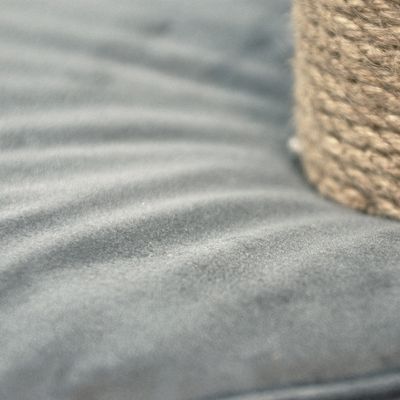 Primo piano di tessuto grigio e di un cordoncino in fibra naturale. La struttura del materiale è chiaramente visibile.