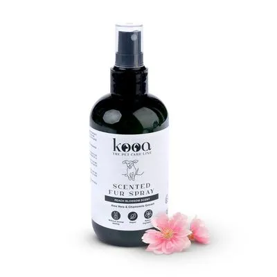 Frasco de spray kooa Scented Fur Spray, aroma Peach Blossom, com extrato de aloé vera e camomila. Rótulo visível em inglês. Flores cor-de-rosa ao lado do frasco.