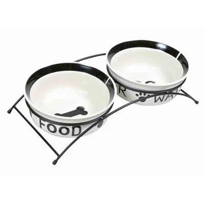 Deux gamelles en céramique blanche avec rebord noir, inscriptions visibles : FOOD et WATER, posées sur un support métallique noir.
