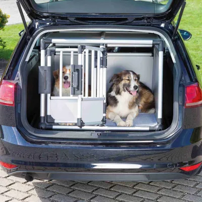 Dwa psy siedzą w srebrnej metalowej klatce transportowej w bagażniku samochodu. Klatka posiada kraty oraz drzwi z zamkiem. Dwa psy siedzą w srebrnej metalowej klatce transportowej w bagażniku samochodu. Klatka posiada kraty oraz drzwi z zamkiem.