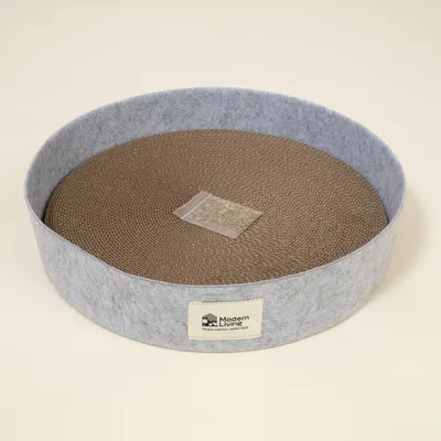 Tapis à griffer rond en carton avec bord en feutre gris, sachet de mélange d’herbes au centre, étiquette Modern Living visible. Tapis à griffer rond en carton avec bord en feutre gris, sachet de mélange d’herbes au centre, étiquette Modern Living visible.