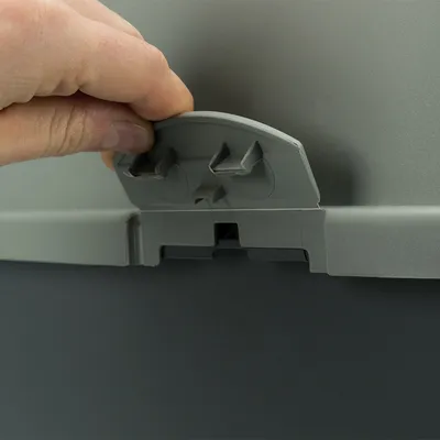 Hand öffnet einen grauen Verschlussmechanismus an einem Behälter. Detailansicht des Clips zur sicheren Verriegelung.