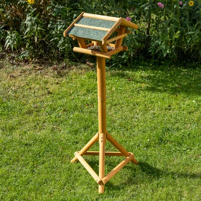 Vogelhaus aus Holz mit grünem Dach und Futterbereich, auf einem stabilen Standfuss im Garten platziert.