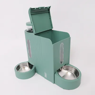 Distributore di cibo verde con due ciotole in acciaio inox e finestre trasparenti. Coperchio superiore aperto, mostra spazio per cibo secco o accessori.