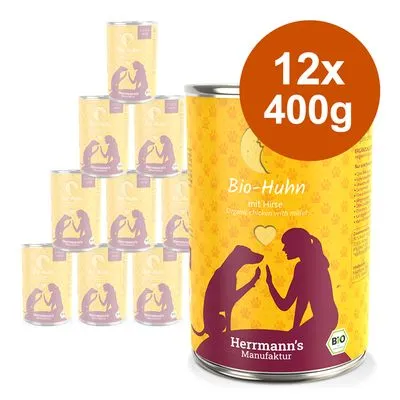 Herrmann's Manufaktur Bio-Huhn met Hirse, 12 blikken à 400g. Gele verpakking met paarse silhouetten van hond en persoon. Tekst: Bio-Huhn mit Hirse, Herrmann's Manufaktur, Bio-keurmerk.