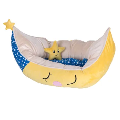 Cama para mascotas en forma de luna amarilla con detalles de estrellas blancas sobre fondo azul y cojín en forma de estrella sonriente. Material textil visible.