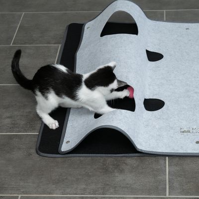 Felt play mat with multiple openings, cat playing with pink toy through one opening. Mat on grey floor.