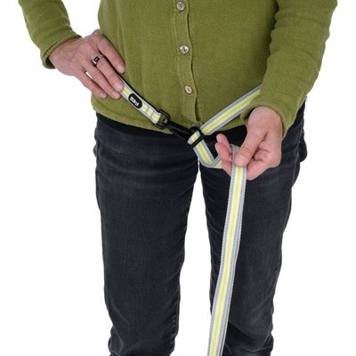 Prezentacja użycia żółto-białego, paskowanego pasa dla psa z klamrą, trzymanego przez osobę.