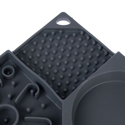 Gros plan sur un plateau compartimenté en plastique gris avec différentes zones texturées à picots et motifs, trou d’accroche visible dans un coin.