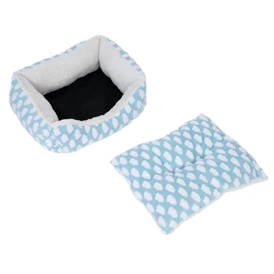Cama para mascotas azul claro con estampado de nubes blancas y cojín extraíble. Forro interior de material suave, base negra visible.